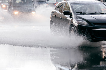 blurred car flow during rainy day. rain water splashing from car wheels on flooded road.
