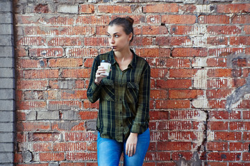 Fototapeta na wymiar young brunette woman in a green plaid shirt drinking coffee