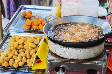 A delicious-looking spicy fried food or fried chicken patty from a boiling pan of a roadside food stall in Thailand