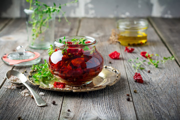 Sun dried tomatoes with thyme and sea salt in an olive oil in a glass jar on the old wooden background. Selective focus.