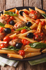 Tasty penne with meatballs, olives and tomato sauce closeup. vertical
