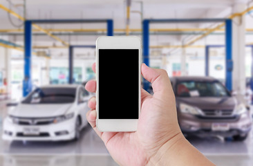 Hand man using smartphone with white screen on blur image of auto repair service as background.