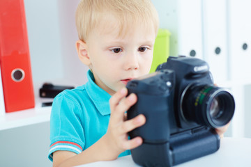 Little boy playing with a camera on the background of office.