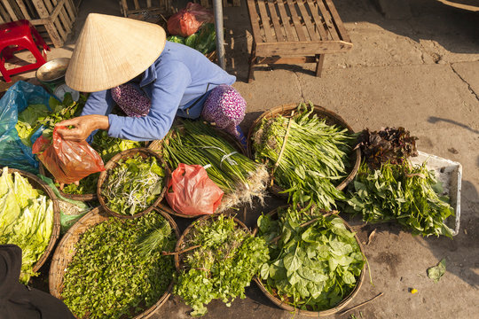 Vietnamese woman with typical conical hat , sell vegetables in a street market