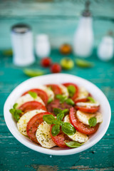 Delicious caprese salad with ripe tomatoes and mozzarella cheese with fresh basil leaves. Italian food. 