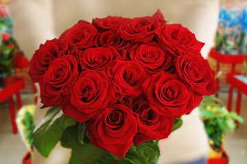 Female hands with beautiful bouquet of red roses on flower shop background