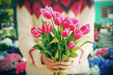 Female hands with beautiful bouquet of tulips on flower shop background
