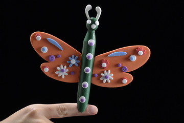 Mano de niño sujeta juguete, hecho por él, con forma de mariposa. Aislado en fondo negro.