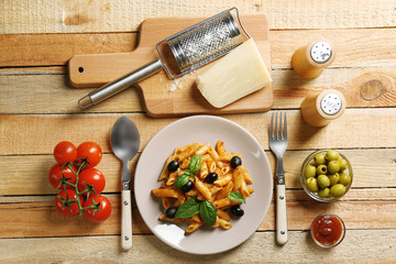 Delicious penne pasta with ingredients on wooden table