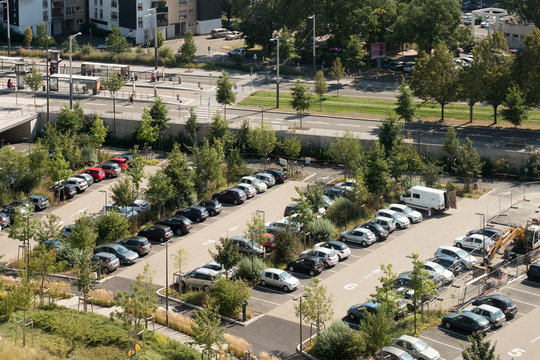 Aerial view of a large parking lot with multiple, cars parked on a summer day - tramway station in the background