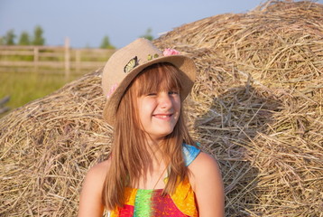 Portrait of naughty, perky, funny little girl with hat on background of haystacks