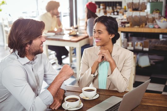 Smiling man and woman using a laptop while having cup of coffee