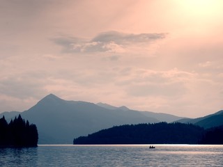 Abandoned fishing paddle boat on Alps lake. Evening lake glowing by sunlight.