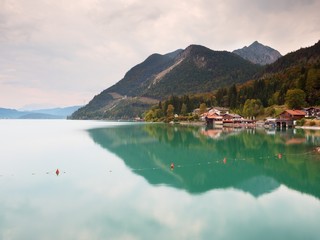Village on the bank of Alps lake. High mountain peaks in mirror of gren water level.