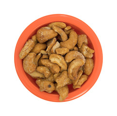 Pieces of honey roasted cashews in an orange bowl isolated on a white background.