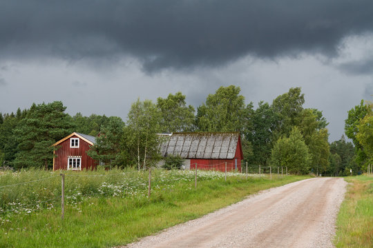 Liten r&ouml;d stuga med med lada vid grusv&auml;g