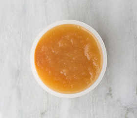 Cinnamon applesauce in a plastic container on a marble table top view.