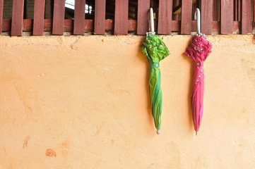 Two old pink and green umbrellas hang on cement and wood wall