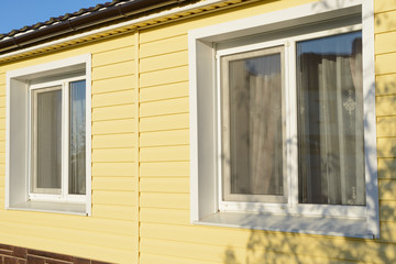 wall of the house with two windows coated with yellow siding