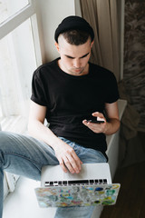 Young male in black t-shirt using his cellphone and laptop