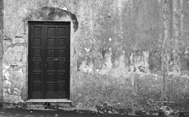  Black and white detail of a side door on an old rusty neighborhood, Italy