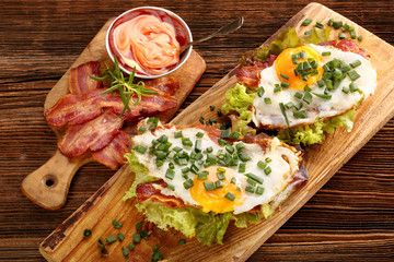 Sandwich with fried bacon, egg and vegetables on wooden backgrou