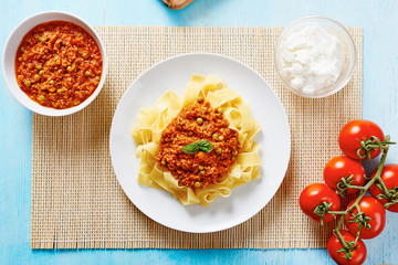 Tagliatelle with Bolognese sauce in white dish surrounded by ricotta cheese, fresh tomatoes, Bolognese sauce in a white bowl on blue table