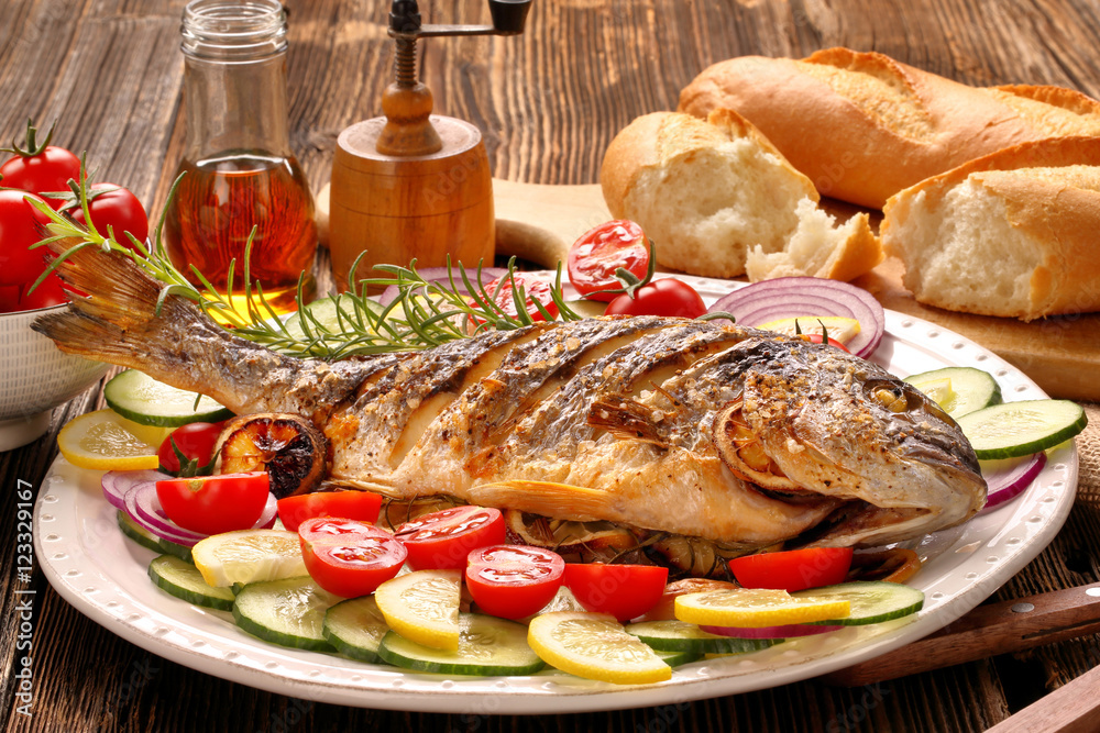 Wall mural Grilled fish with baguette and vegetables on the plate