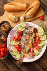Grilled fish with baguette and vegetables on the plate