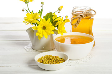 the jar of honey near two bowls, one with  of pollen another wit