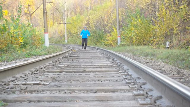 Man Jogging Train Tracks Railway in Autumn Season in forest. Training and exercising outdoors when cross country running in inspirational autumn  landscape. Sports Motivation.