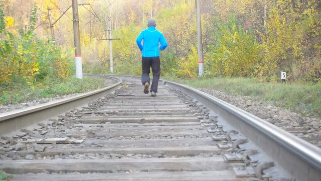 Man Jogging Train Tracks Railway in Autumn Season in forest. Training and exercising outdoors when cross country running in inspirational autumn  landscape. Sports Motivation.