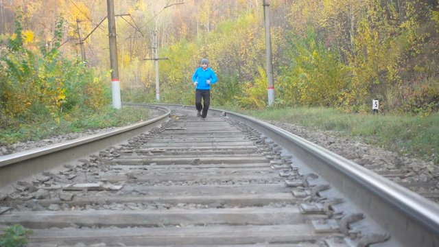 Man Jogging Train Tracks Railway in Autumn Season in forest. Training and exercising outdoors when cross country running in inspirational autumn  landscape. Sports Motivation. Slow Motion.