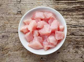 Raw cut chicken fillet in white bowl, from above