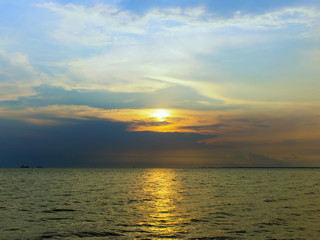 Sunset or sunrise over the ocean with some ship near the peer.