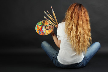 Fototapeta premium Girl painter with a palette and brushes on a dark background. 