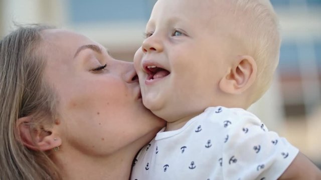 Close up of happy mother snuggling and kissing cheek of laughing blond baby