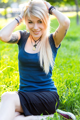 Portrait of beautiful young blonde with long hair sitting in a Park on the grass