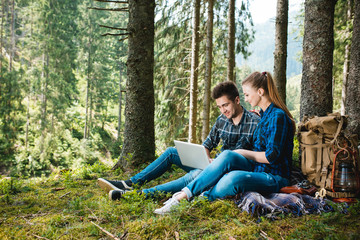 A guy and a girl tourists relax in the mountain forest, sitting and looking at laptop