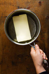 piece of butter in a pan . female hand