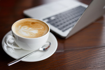 Cup of cappuccino and laptop on the table in cafe