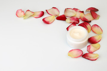 Fototapeta na wymiar Still life with cream jar and rose petals on white background.