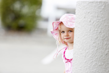 Adorable little caucasian girl in nice hat looking out of the white column