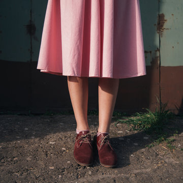 Close up of beautiful legs in shoes and pink dress of a young woman