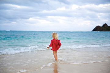 Fototapeta na wymiar Little girl in red coat running into the water on the beach