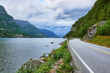 The norwegian road Route 13 in Hordaland running on the edge of the inlet Sandvevatnet on a gray overcast afternoon in Norway
