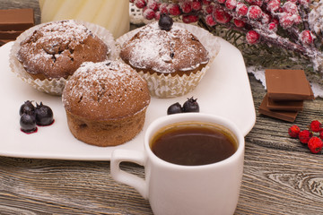 cupcake with berries on a white plate, chocolate, candle, small white cup of coffee, snowy fir branch on wooden background