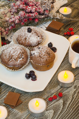 cupcake with berries on a white plate, chocolate, candle, small white cup of coffee, snowy fir branch on wooden background