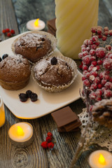cupcake with berries on a white plate, chocolate, candle, small white cup of coffee, snowy fir branch on wooden background