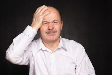 Older man in white shirt hugged his head, wincing.